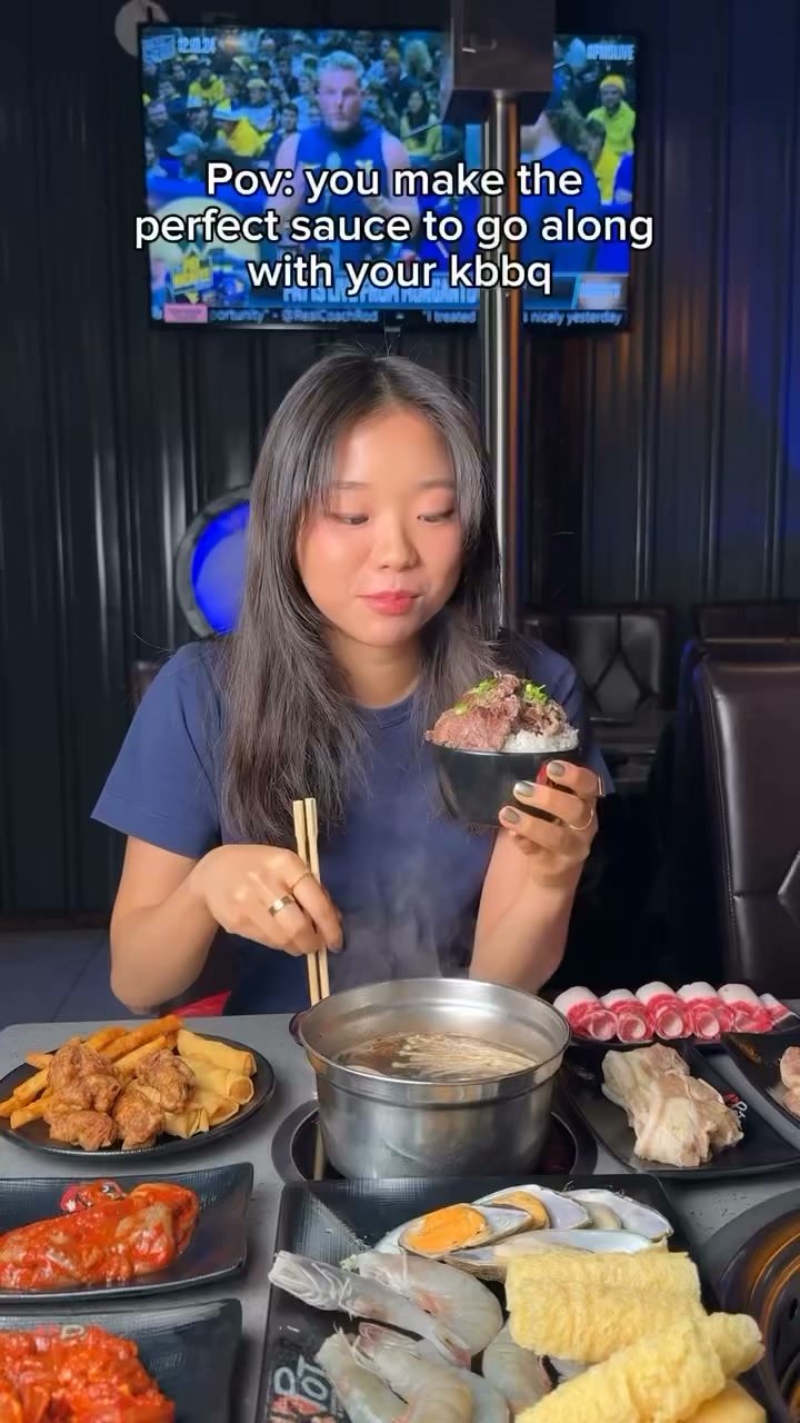 A guest at KPOT Middletown lifting a bowl of grilled beef over rice beside a simmering hot pot in the dining room