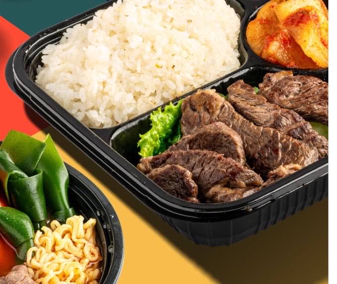 A KPOT 2 GO bento box with grilled beef, white rice and kimchi beside a bowl of hot pot noodles and vegetables